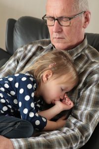 A grandfather holding his granddaughter and having a nap.