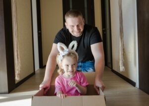 A little girl with bunny ears playing with her father in a cardboard box. 
