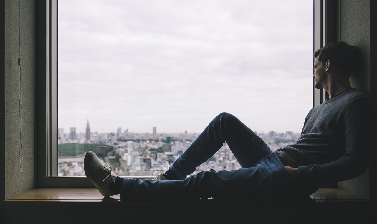 A man sitting by the window and looking at the cityscape. 